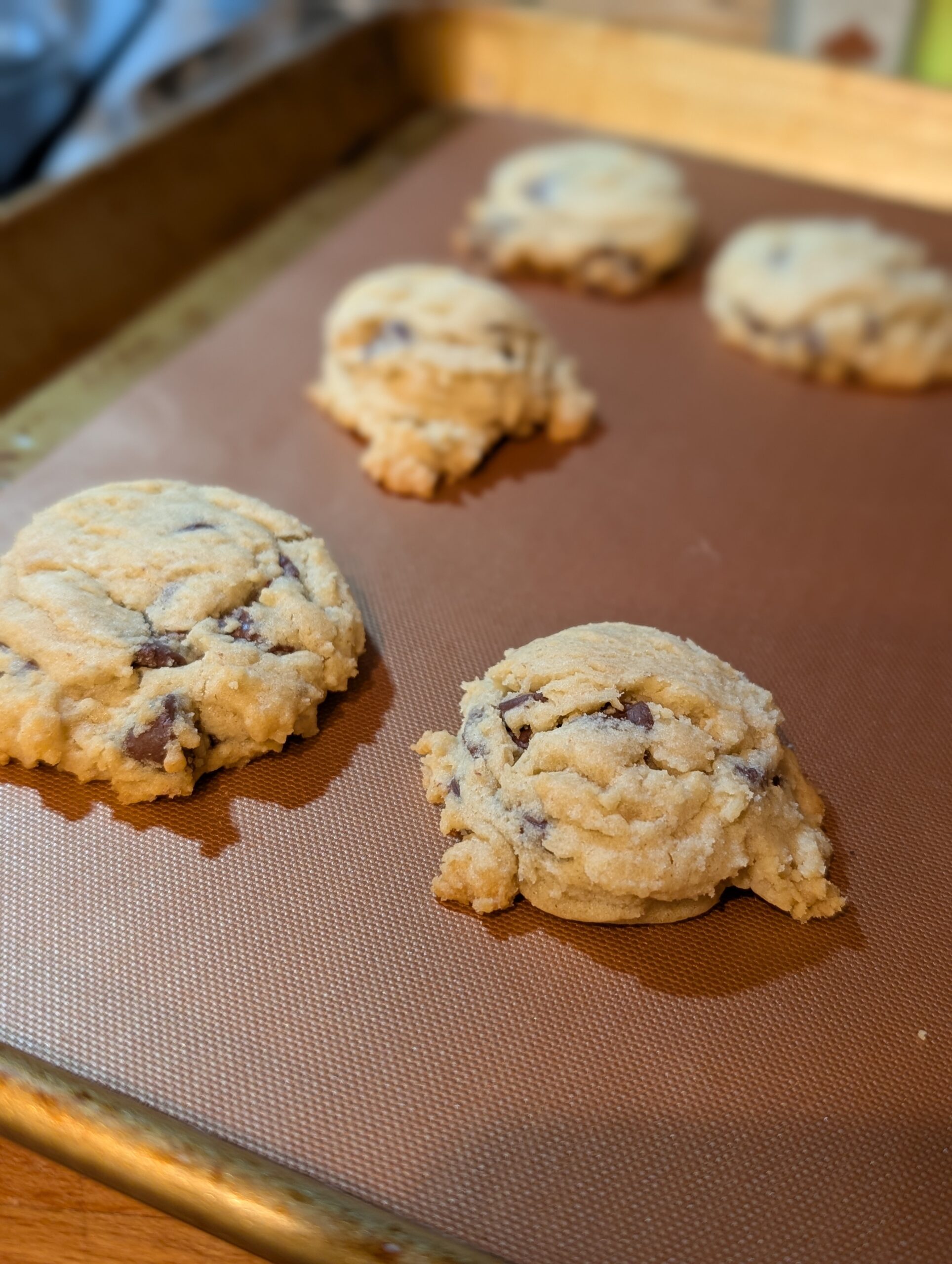 Freshly baked chocolate chip cookies on a baking sheet with a silicone mat.