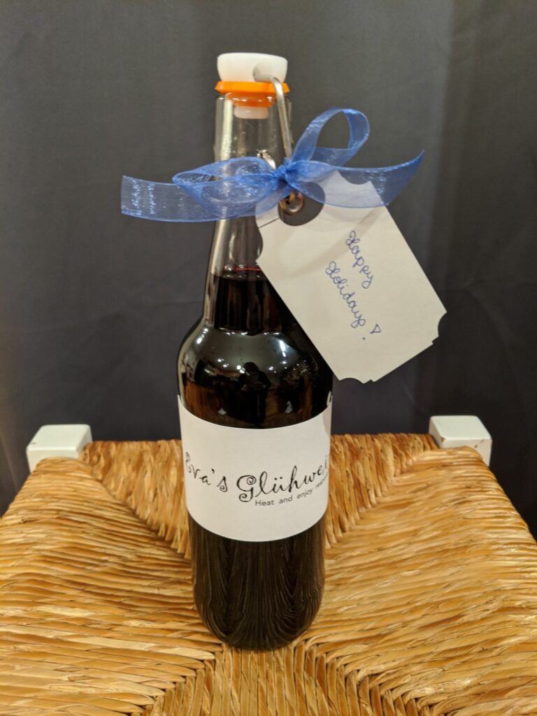 Homemade Glühwein bottled in a swing-top glass bottle, decorated with a blue ribbon and a handwritten gift tag that reads “Happy Holidays !"