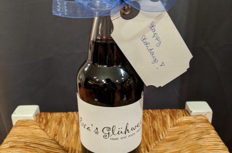 Homemade Glühwein bottled in a swing-top glass bottle, decorated with a blue ribbon and a handwritten gift tag that reads “Happy Holidays !"